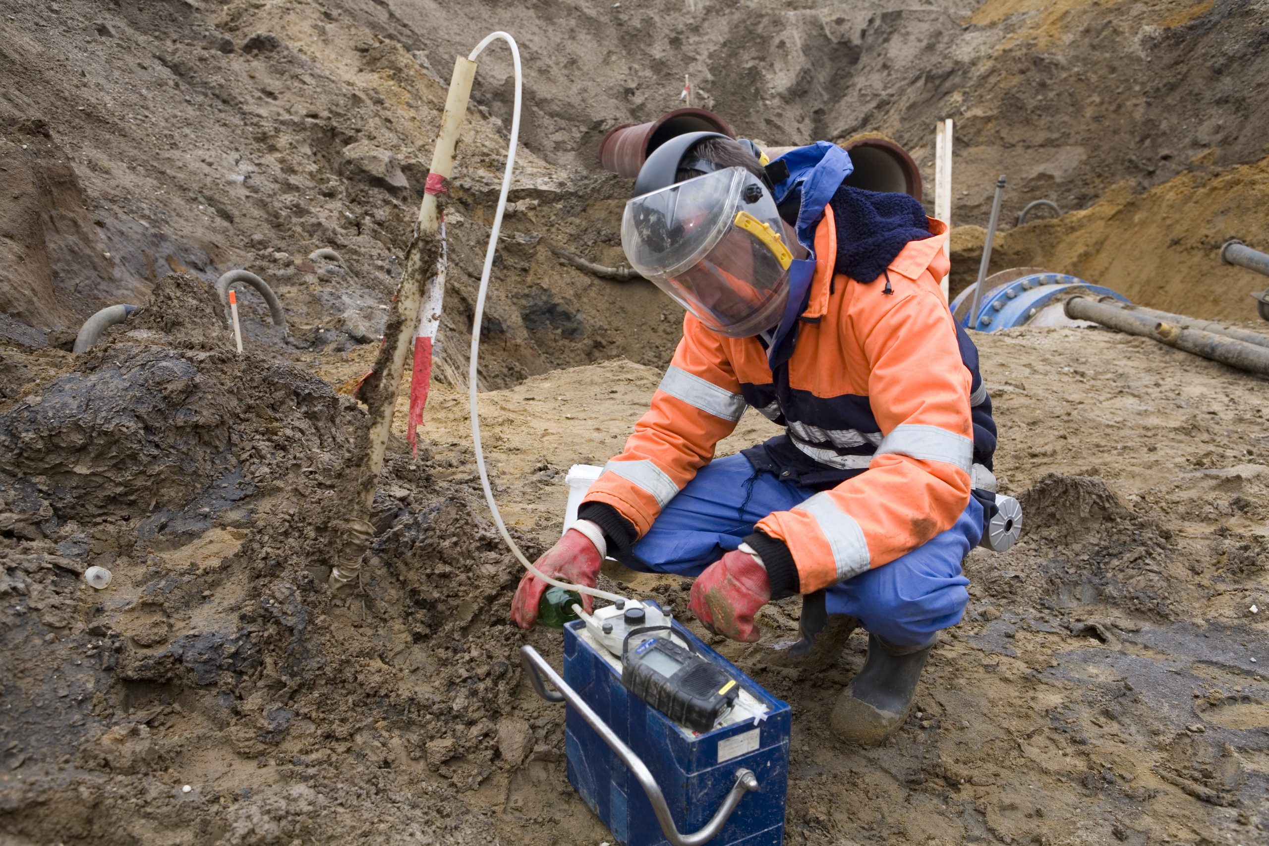 Mann im Anzug bei der Probenahme aus einem Erdhaufen auf einer Baustelle
